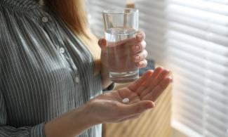 Eine Frau mit einer Pille und einem Glas Wasser in den Händen