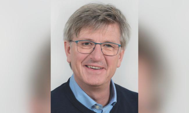 Ein Mann mit grauen Haaren und einer Brille, er lächelt