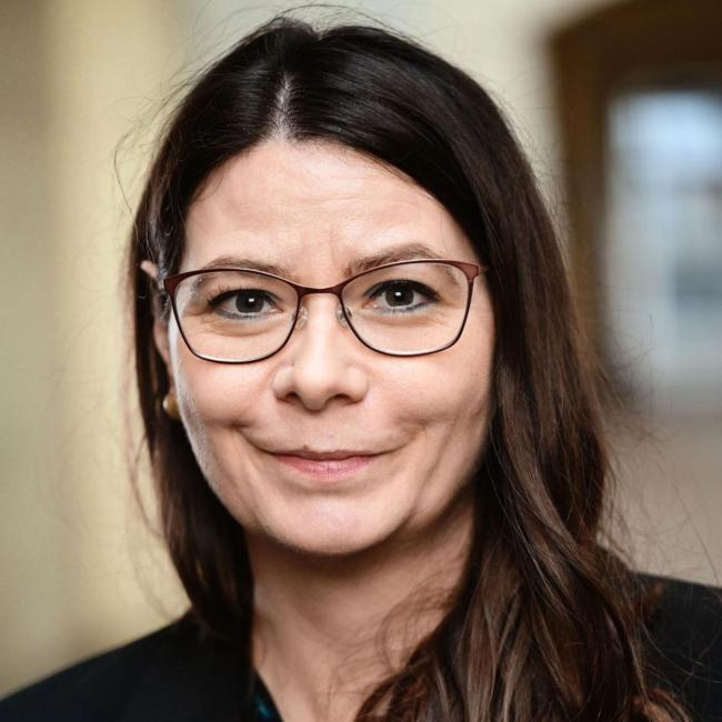 Eine Frau mit dunklen langen Haaren und Brille lächelt in die Kamera