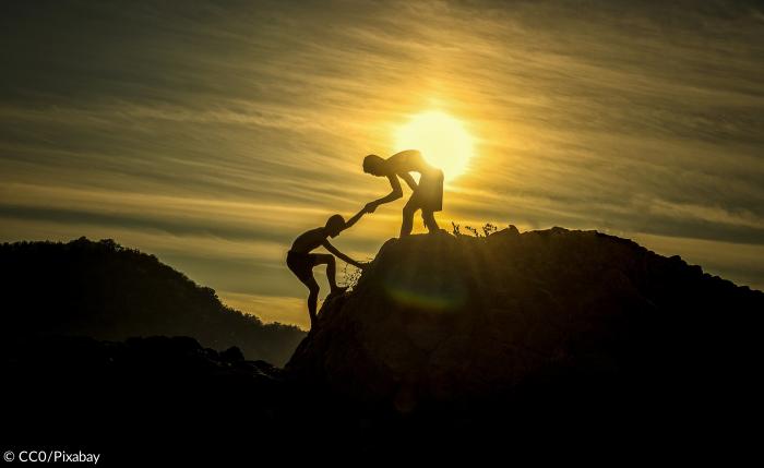 Zwei Jungen helfen sich gegensetig einen Berg zu erklimmen 
