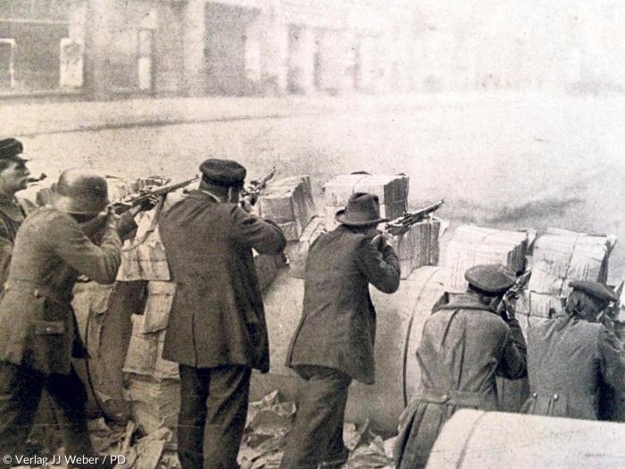 Stahlhelm, Mütze, Hut – Revolutionäre hinter Barrikaden aus Zeitungsstapeln: Im Berliner Zeitungsviertel wurde während des Spartakusaufstands im Januar 1919 besonders heftig gekämpft.