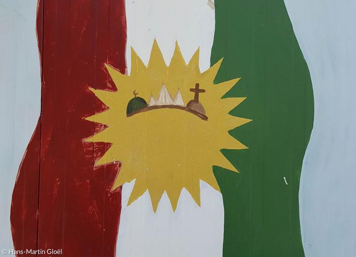 Traum von einer Versöhnung der Religionen: die Kurdische Flagge, in der Sonne die Symbole der Muslime, der Jesiden und der Christen.