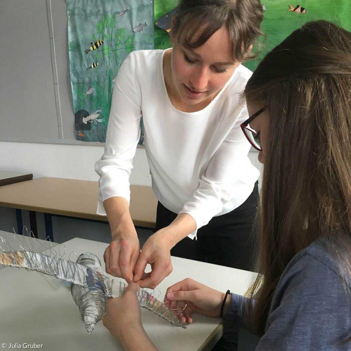Die Künstlerin Miriam Maria Ferstl hilft einer Schülerin, die Tauben aus Pappmaschee mit Draht zu umwickeln. 
