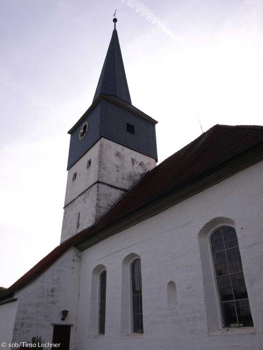 Die Außenfassade der Evangelischen Kirche Weisendorf aus einem anderen Winkel. man sieht den Kirchturm und ein schräges Dach.