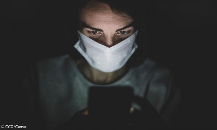 Eine Frau mit einer Maske, die auf einen Handybildschirm blickt.