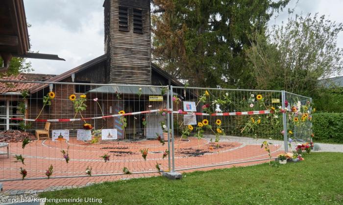 Die abgebrannte Kirche in Utting, umgeben von einem Bauzaun, der mit Sonnenblumen dekoriert ist.