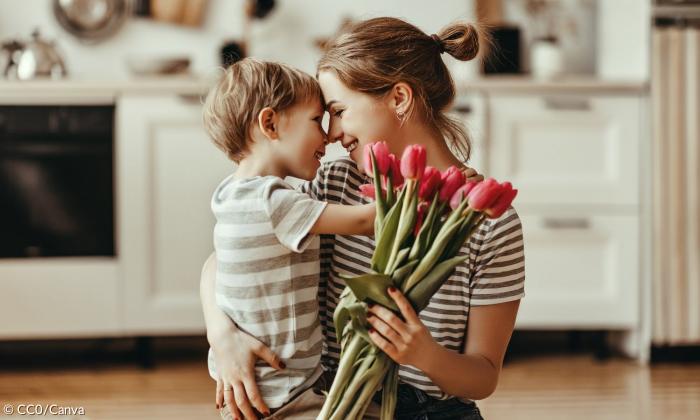 Eine Mutter umarmt ihr Kind und hat einen Blumenstrauß in der Hand