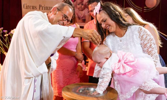 Ein Pfarrer tauft ein Baby in der Manege eines Circus'