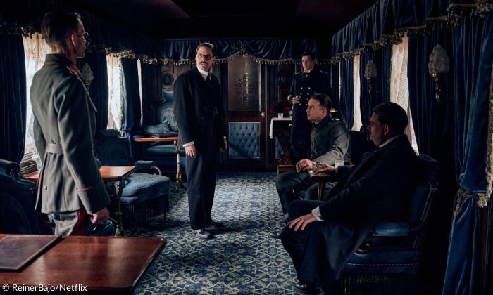 Szene aus dem Film: In einem Zug wird der Waffenstillstand verhandelt. Es befinden sich fünf Männer im Raum. Der Raum ist vor allem blau dominiert. Alle tragen Uniform.