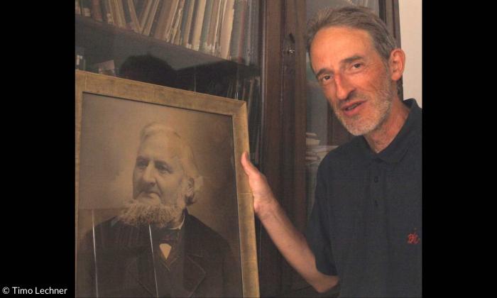 Universitätsmusikdirektor Konrad Klek mit dem Porträt Johann Georg Herzogs vor seinem Bücherschrank im Erlanger Büro.