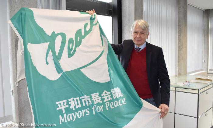 Ein Mann hält eine Fahne, auf der "Mayors for Peace" steht