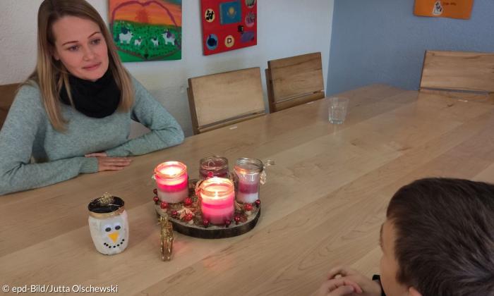 Eine Frau sitzt an einem Tisch mit Kerzen, ihr gegenüber ein Junge, den man nur von hinten sieht