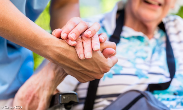 Ein Pfleger hält die Hand einer im Rollstuhl sitzenden Seniorin.