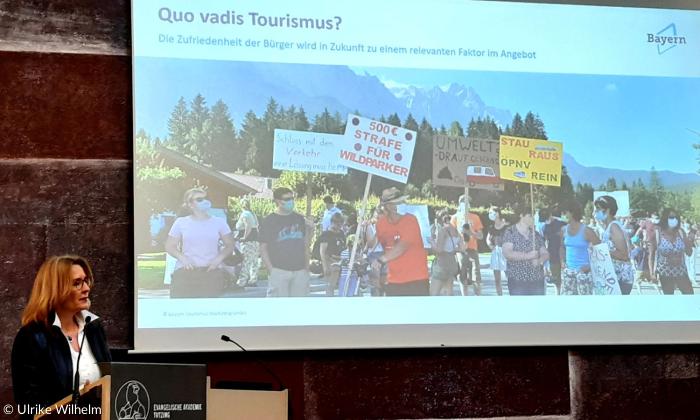 Eine Frau am Rednerpult, hinter ihr eine Präsentation mit der Überschrift "Quo vadis Tourismus?"