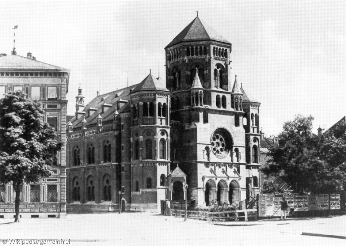 Auf dem Schwarz-Weiß-Bild erkennt man einen Flügel sowie die Front einer großen Synagoge. Links neben ihr bahnt sich ein weiteres großes Haus an. 