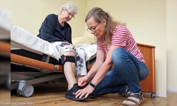 Eine Pflegerin zieht einer Patientin Schuhe an