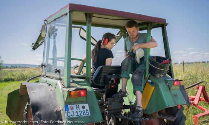 Eine Frau und ein Mann sitzen auf einem Traktor und schauen auf einen Controller.