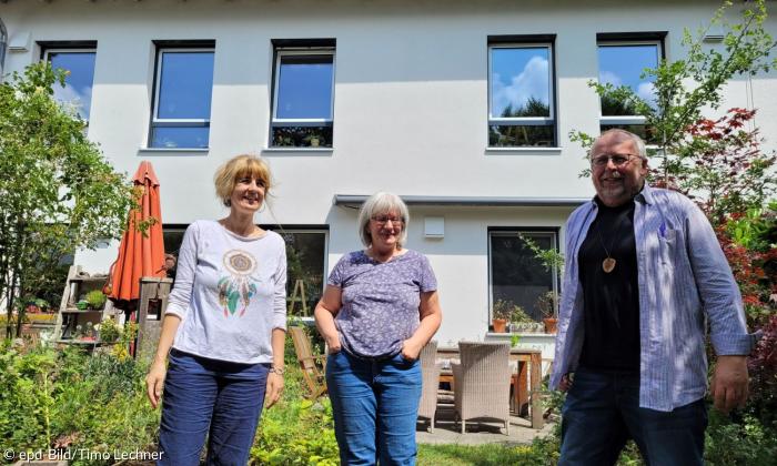 Zwei Frauen und ein Mann stehen vor einem Haus