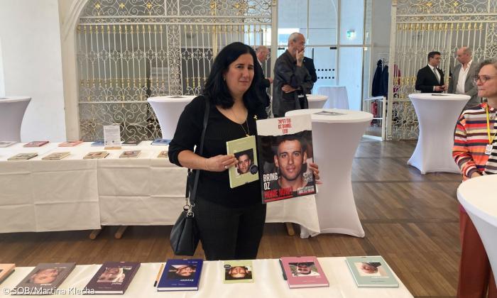 Eine Frau hält ein Buch und ein Plakat in die Kamera