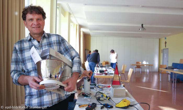 Ein Mann hält eine reparierte Küchenmaschine in die Kamera