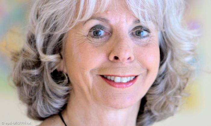 Eine Frau mit weiß-grauen Haaren lächelt in die Kamera
