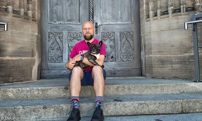 Ein Mann mit Hund auf dem Arm vor einer Kirchentür