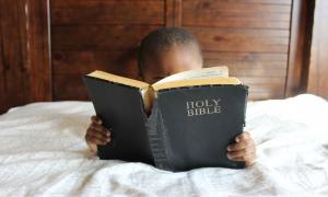 Kind liest Bibel im Bett.