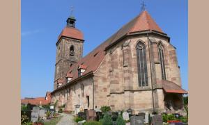 Die evangelische Kirche St. Laurentius in Roßtal. Die Kirche ist aus braunen Steinen gebaut und hat einen Kirchturm mit einer welsche Haube.