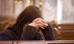 Eine Frau betet in einer Kirche, die Hände vor dem Gesicht gefaltet
