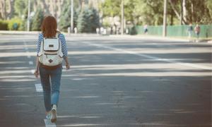 Eine junge Frau läuft am Rand einer Straße. Sichtbar ist nur ihr Rücken, auf dem sie einen Rucksack trägt.