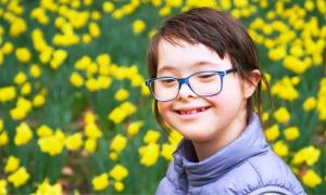 Ein Mädchen mit Down-Syndrom lächelt vor einem Blumenfeld.