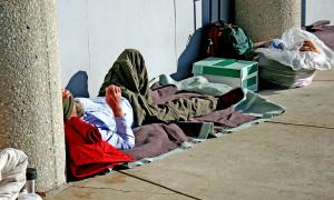 Ein obdachloser Mann liegt auf einer Decke in der prallen Sonne