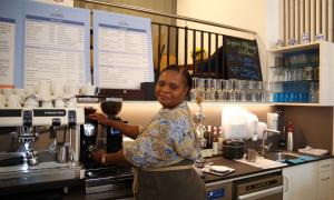 Eine schwarze Frau steht an der Kaffeemaschine und lächelt