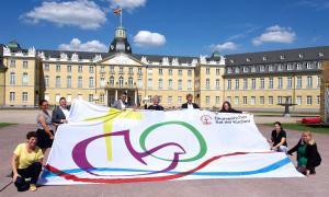 Menschen halten eine Fahne mit dem ÖRK-Logo vor dem Schloss Karlsruhe