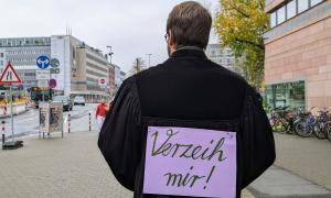 Der Nürnberger Dekan Jonas Schiller in Nürnberg. Er trägt einen Talar und steht mit dem Rücken zur Kamera. Darauf ist ein lila Schild geklebt, auf dem "Verzeih mir" steht