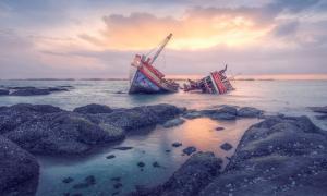Ein zerborstenes Schiff im Meer, davor Felsen