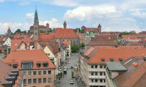 Aus einem Fenster im vierten Stock wurde ein Bild über Nürnberg gemacht. Man erkennt viele Ziegeldächer und ganz hinten die Burg Nürnbergs. 