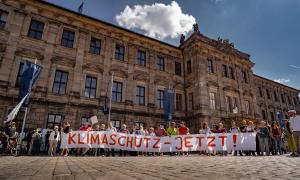 "Kilmaschutz Jetzt" steht auf einem Banner, das mehrere Menschen vor einem Universitätsgebäude hochhalten. 