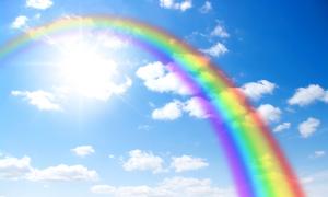 Ein Regenbogen erstreckt sich von der linken oberen Ecke zur rechten unteren Ecke über das ganze Bild. Hinter ihm sind die strahlende Sonne, Wolken und blauer Himmel zu erkennen. 