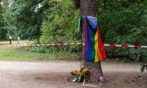 Eine Regenbogenfahne und Blumen an einem Baum