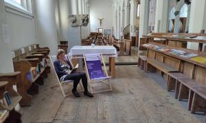 Eine Frau sitzt in einem von zwei Liegestühlen, die in einer Kirche stehen, und liest